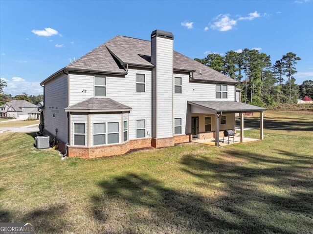 rear view of property with a patio, a chimney, a shingled roof, and a lawn