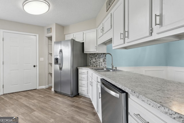 kitchen featuring appliances with stainless steel finishes, light countertops, white cabinets, a sink, and a textured ceiling