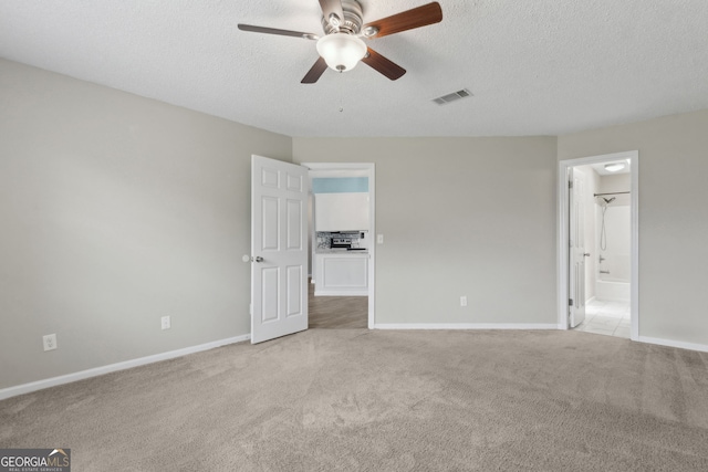 unfurnished bedroom featuring connected bathroom, visible vents, light carpet, baseboards, and a textured ceiling