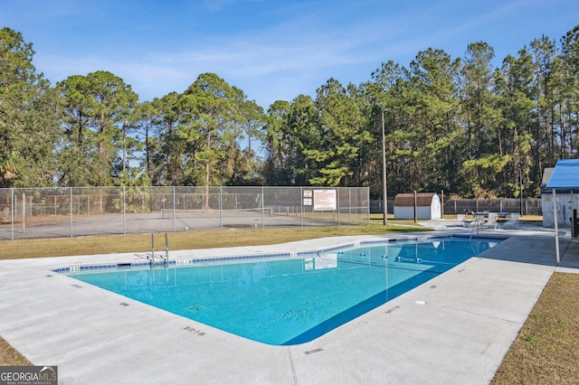 pool featuring a patio, fence, a shed, and an outbuilding