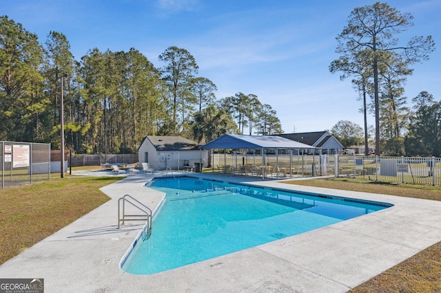 community pool with a patio, a lawn, and fence