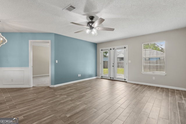 spare room featuring visible vents, a wealth of natural light, wood finished floors, and ceiling fan with notable chandelier