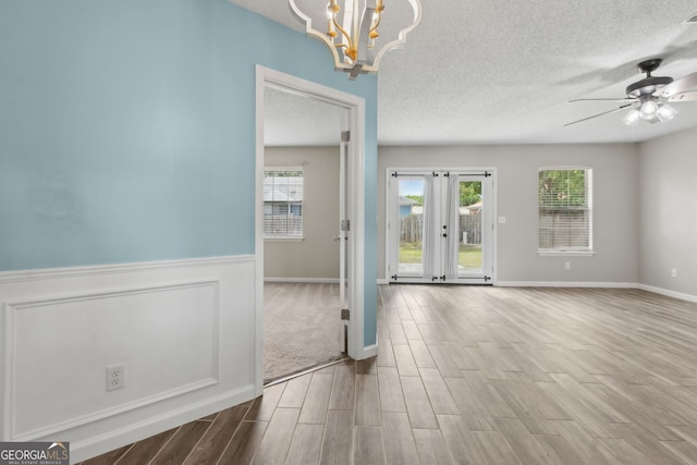 spare room with a wealth of natural light, wood finished floors, ceiling fan with notable chandelier, and a textured ceiling