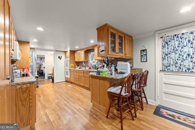 5855 Willis Ln, Cumming, GA 30040 - kitchen with decorative backsplash, light wood-style flooring, glass insert cabinets, a breakfast bar, and recessed lighting