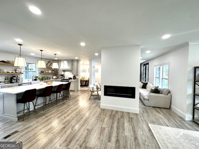 living room with visible vents, light wood-type flooring, crown molding, and recessed lighting