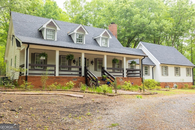 cape cod home featuring a shingled roof, a chimney, and a porch