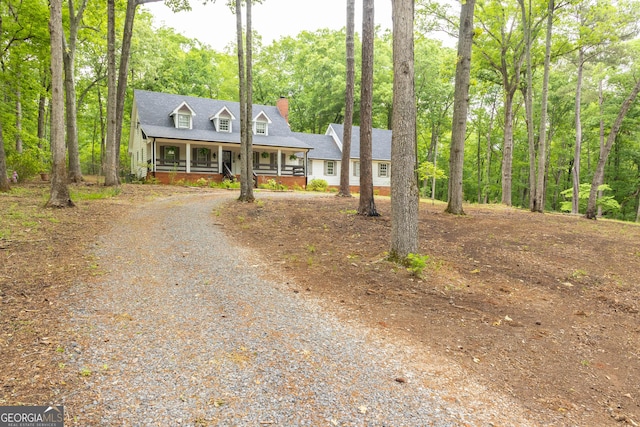 new england style home with a chimney, a porch, and gravel driveway