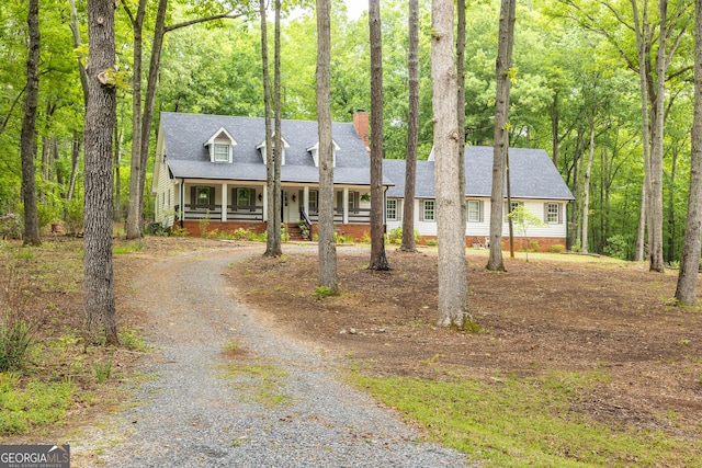new england style home with a shingled roof, a porch, a chimney, and driveway