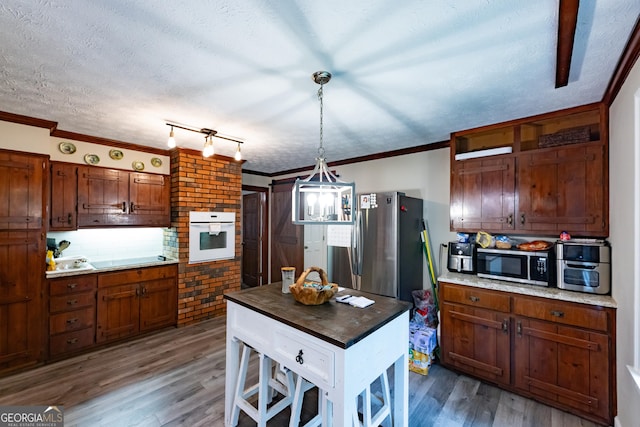 kitchen featuring crown molding, oven, stainless steel microwave, and wood finished floors