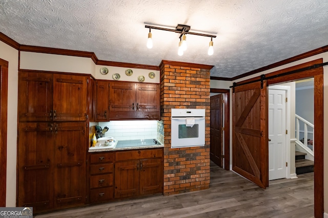 kitchen with a textured ceiling, wood finished floors, a barn door, and oven