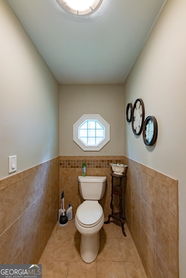 bathroom with tile patterned flooring, wainscoting, toilet, and tile walls