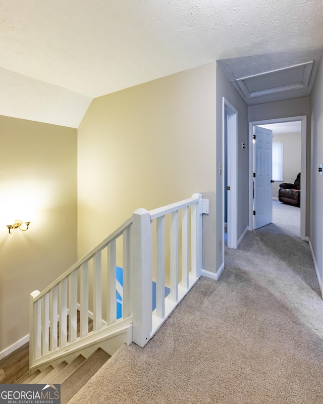 hall featuring carpet floors, baseboards, an upstairs landing, and attic access