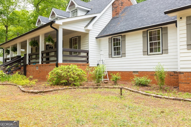 view of side of property with covered porch, a shingled roof, and crawl space