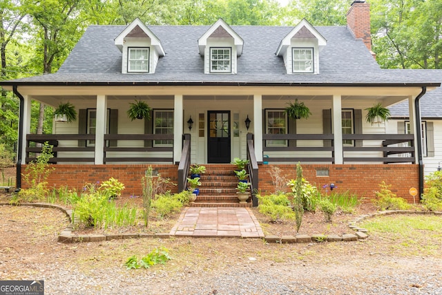 view of front of home featuring roof with shingles, covered porch, and a chimney