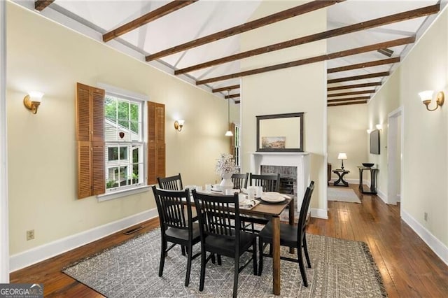 dining room with visible vents, a fireplace, hardwood / wood-style floors, baseboards, and vaulted ceiling with beams