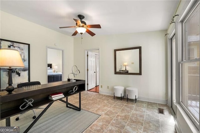 office with visible vents, a ceiling fan, baseboards, and stone finish floor