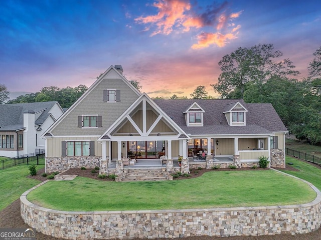 rear view of house with a patio, a lawn, stone siding, board and batten siding, and fence