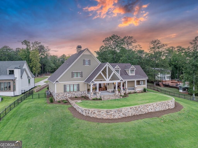 back of house at dusk with a lawn, a fenced backyard, covered porch, and a chimney
