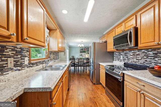 kitchen with a sink, decorative backsplash, light wood-style flooring, a textured ceiling, and appliances with stainless steel finishes