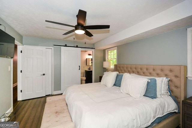 bedroom with ceiling fan, a barn door, baseboards, wood finished floors, and ensuite bath