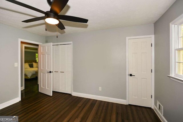 unfurnished bedroom with baseboards, visible vents, wood finished floors, and multiple windows
