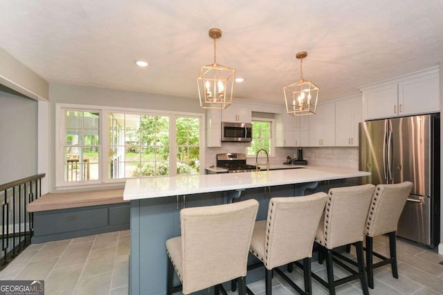 kitchen with a chandelier, stainless steel appliances, light countertops, white cabinets, and backsplash
