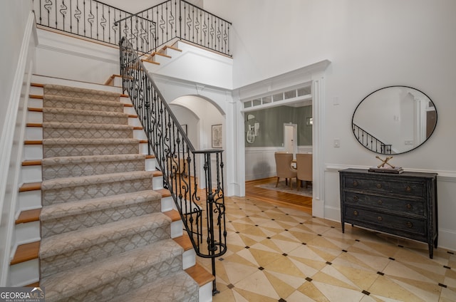8345 Jett Ferry Rd, Sandy Springs, GA 30350 - stairway featuring arched walkways, wainscoting, tile patterned flooring, and a towering ceiling