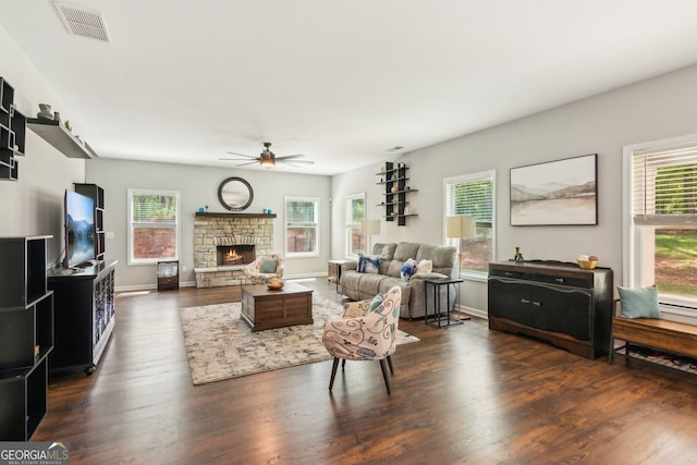 living area featuring a wealth of natural light, visible vents, a ceiling fan, and a stone fireplace