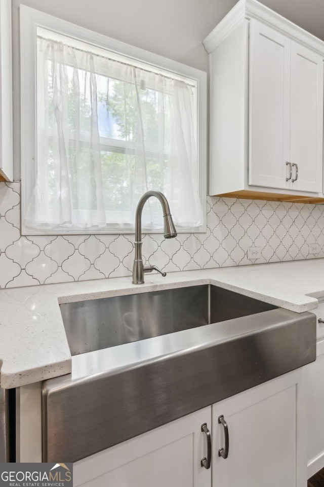 kitchen with white cabinetry, tasteful backsplash, light stone countertops, and a sink