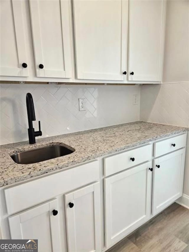 kitchen with light wood-type flooring, a sink, white cabinetry, and decorative backsplash