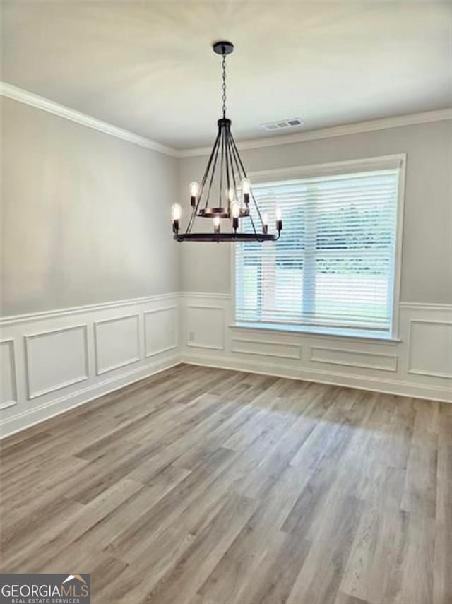 unfurnished dining area with an inviting chandelier, crown molding, visible vents, a decorative wall, and a wainscoted wall