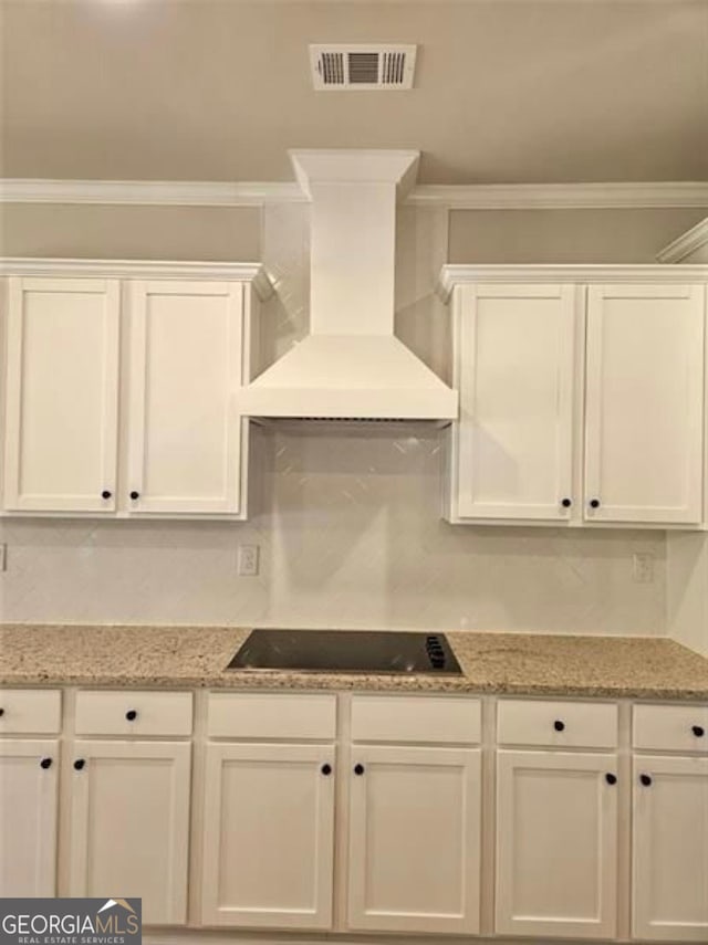 kitchen featuring wall chimney range hood, white cabinetry, visible vents, and black electric cooktop