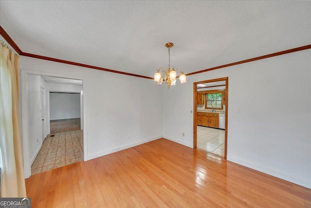 spare room with baseboards, ornamental molding, an inviting chandelier, and light wood-style flooring