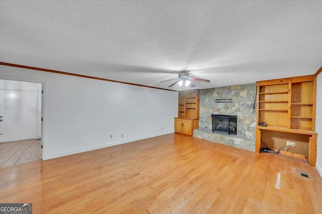 unfurnished living room with wood finished floors, ceiling fan, a stone fireplace, and crown molding