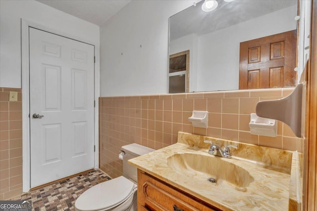 bathroom with tile walls, wainscoting, toilet, and vanity