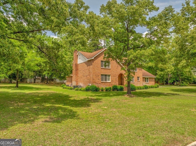 view of side of property featuring a lawn, fence, a chimney, and brick siding
