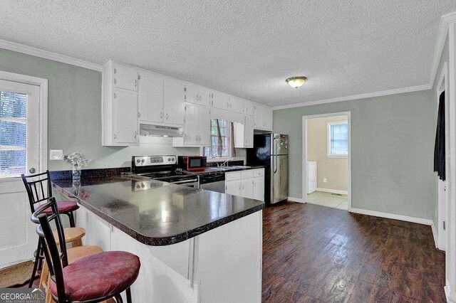 4850 Forest Blvd, Gainesville, GA 30506 - kitchen featuring appliances with stainless steel finishes, under cabinet range hood, dark countertops, dark wood-style floors, and crown molding