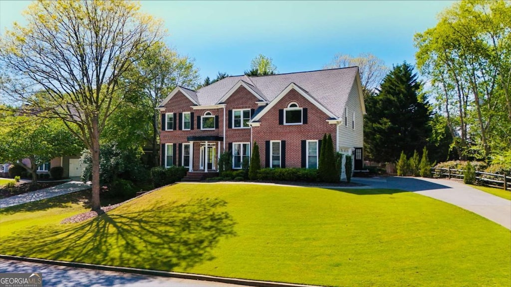 colonial inspired home featuring brick siding, fence, and a front yard