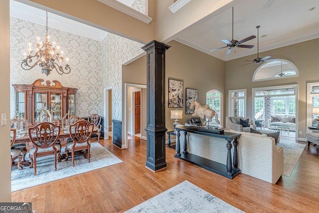 living room with crown molding, a towering ceiling, light wood-type flooring, and ornate columns