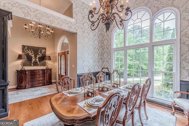 dining area with a notable chandelier, wallpapered walls, wood finished floors, and a healthy amount of sunlight