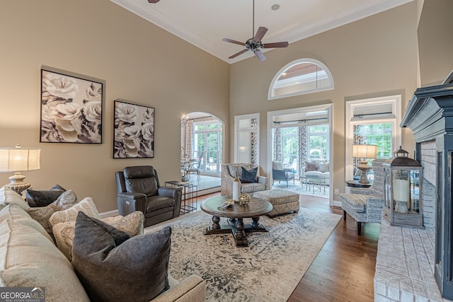 living area featuring wood finished floors, a fireplace with raised hearth, baseboards, a ceiling fan, and crown molding