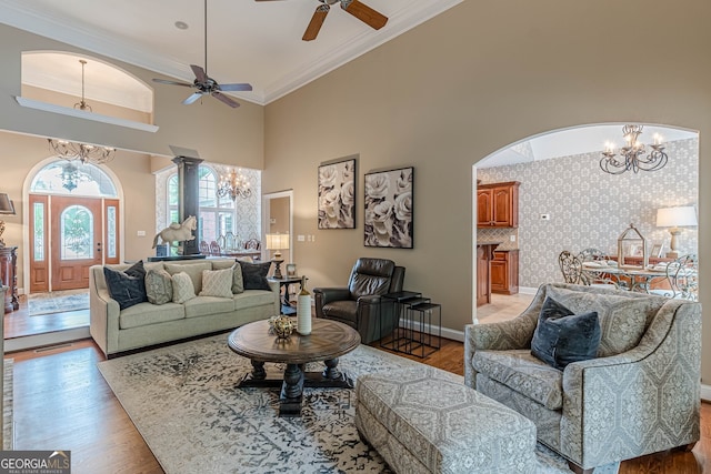 living room featuring arched walkways, light wood-style flooring, ceiling fan with notable chandelier, a high ceiling, and crown molding