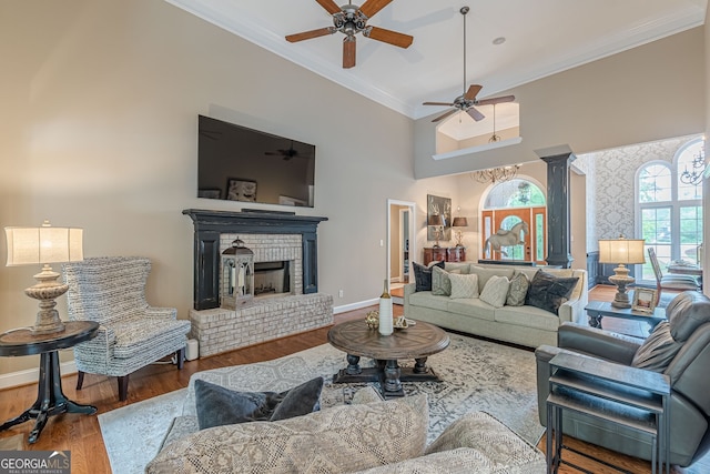 living area with wood finished floors, a fireplace, baseboards, a ceiling fan, and crown molding