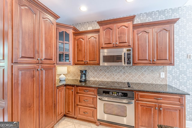 kitchen with dark stone counters, tasteful backsplash, glass insert cabinets, stainless steel appliances, and wallpapered walls