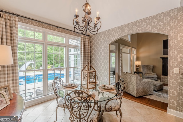 dining room featuring arched walkways, an inviting chandelier, tile patterned floors, wallpapered walls, and baseboards
