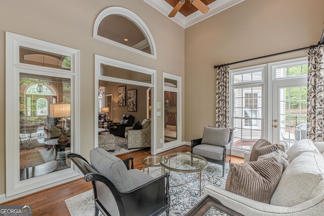 living area featuring a high ceiling, a ceiling fan, baseboards, ornamental molding, and wood finished floors