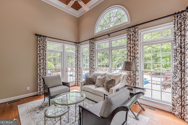 living area featuring visible vents, baseboards, ornamental molding, a towering ceiling, and a ceiling fan