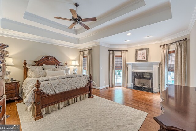 bedroom with crown molding, wood finished floors, a high end fireplace, and a tray ceiling
