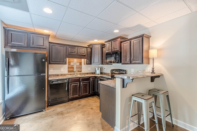 kitchen with a kitchen breakfast bar, a sink, dark brown cabinetry, black appliances, and a peninsula