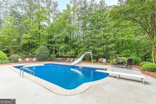 pool featuring fence, a diving board, a water slide, and a patio area
